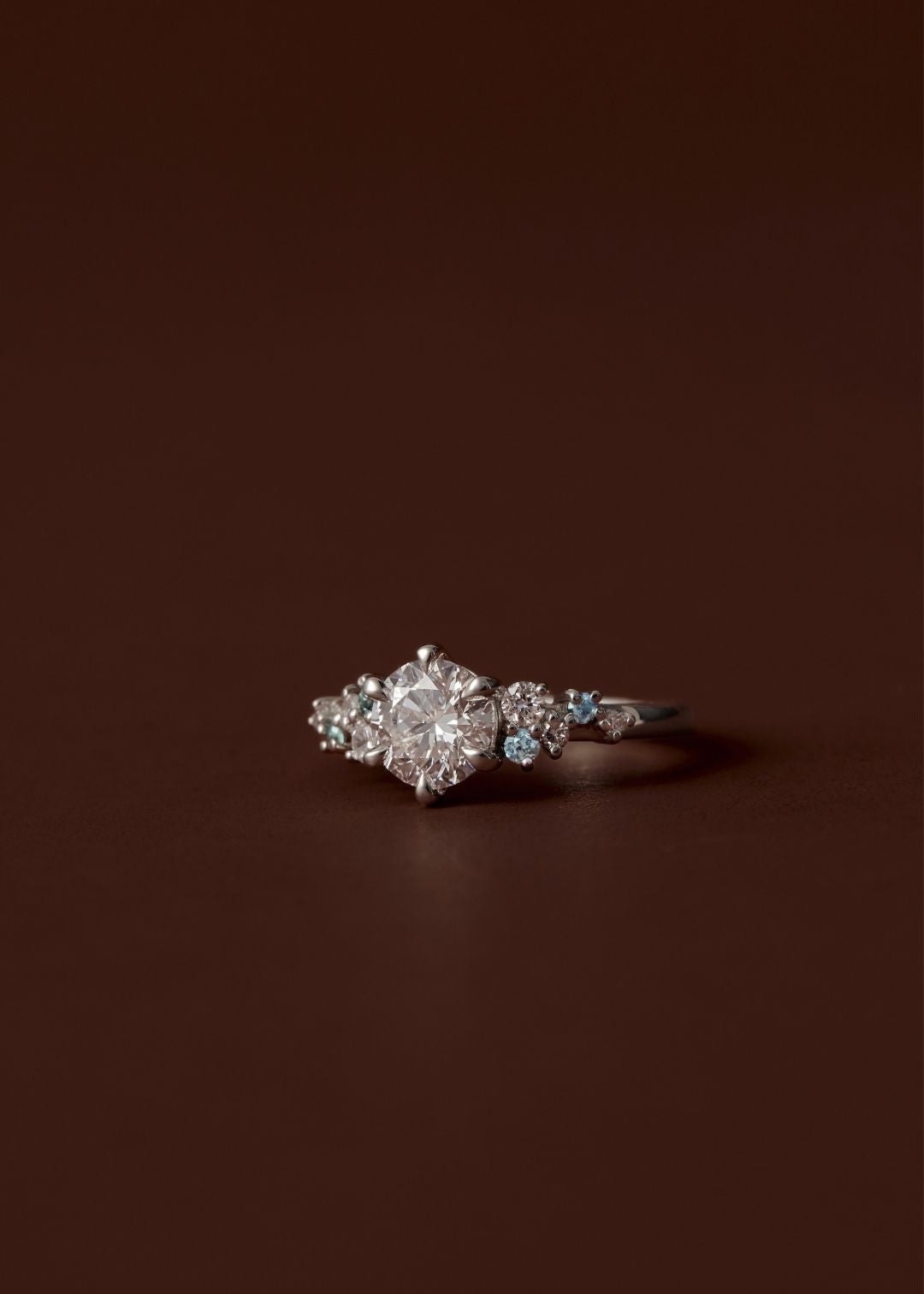 Asymmetrical sapphire and diamond cluster engagement ring with round centre diamond