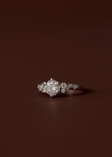 Asymmetrical sapphire and diamond cluster engagement ring with round centre diamond