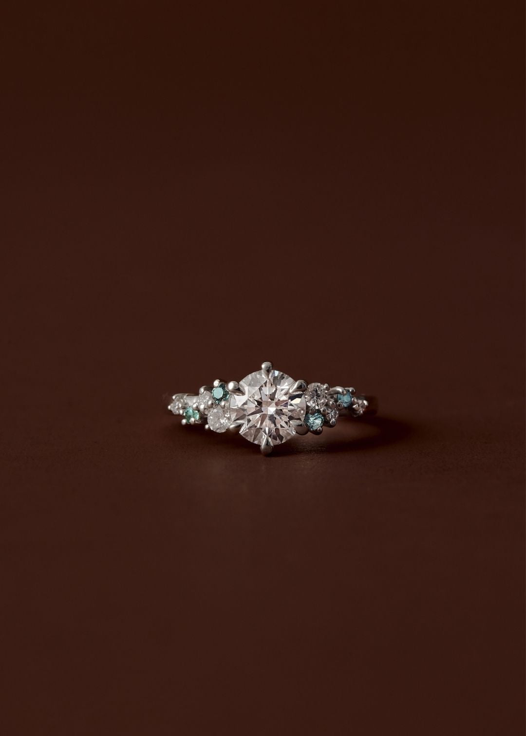 Asymmetrical sapphire and diamond cluster engagement ring with round centre diamond
